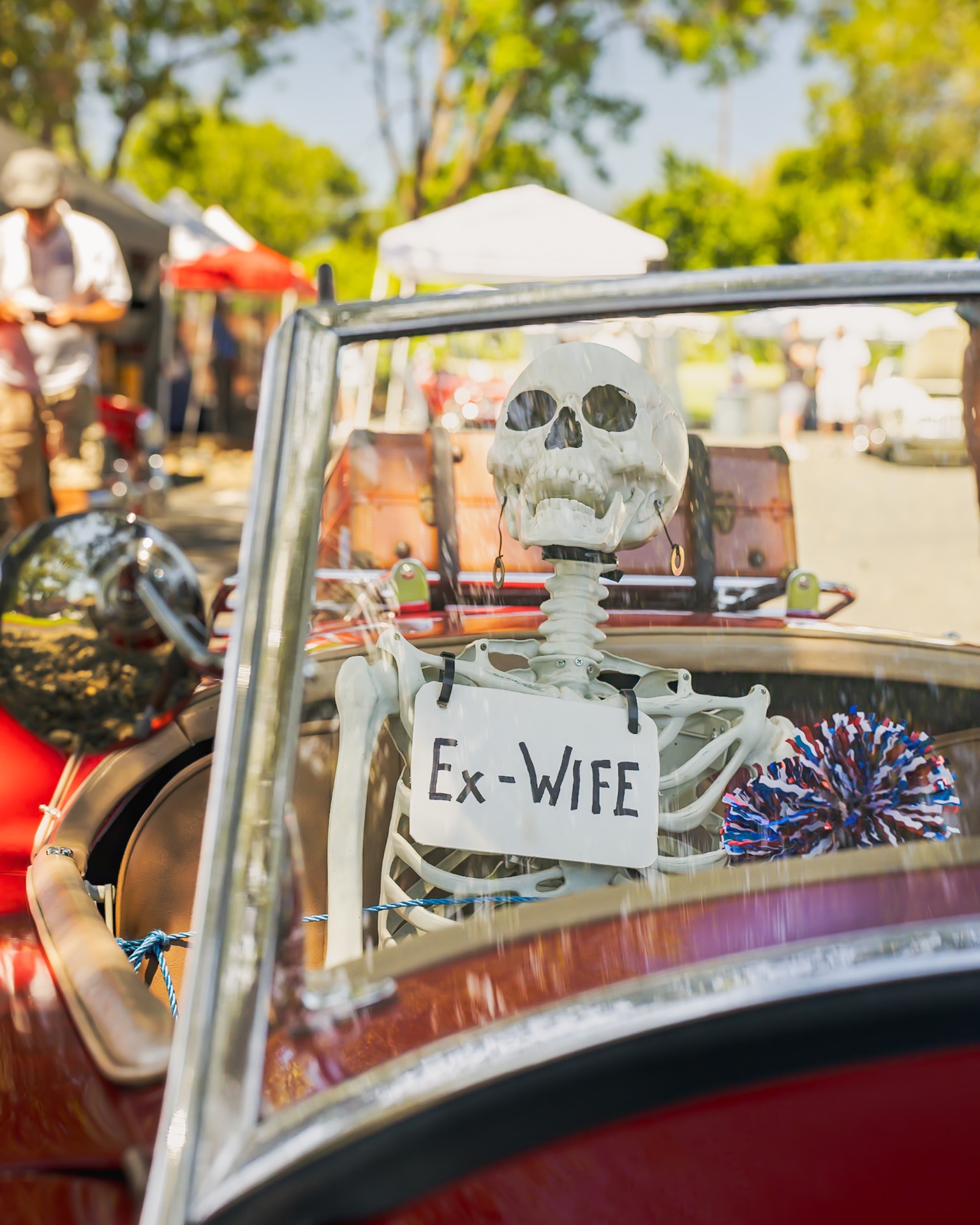 Skeleton passenger with 'Ex-Wife' sign in a classic convertible